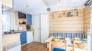Una cocina compacta con microondas, estufa y lavaplatos, un comedor con mesa y sillas, y un banco con cojín a rayas.