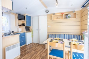 A compact kitchen with a microwave, stove, and sink, a dining area with a table and chairs, and a bench with a striped cushion.