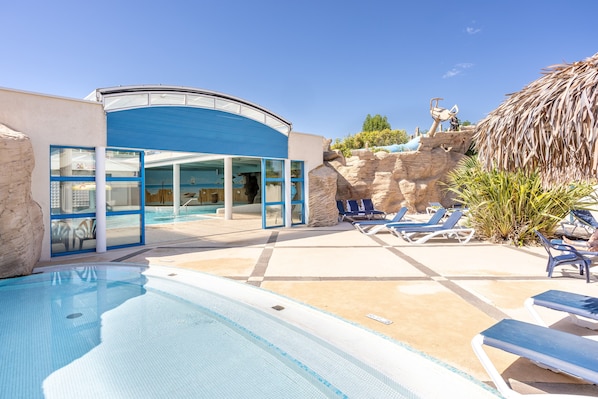 A pool area with lounge chairs, a building with a blue facade, and a thatched roof structure.