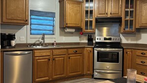 Una cocina moderna con armarios de madera, electrodomésticos de acero inoxidable y un ventanal con persianas azules.