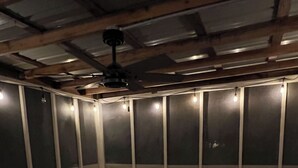 Un espacio al aire libre con un amplio sofá modular y una pequeña mesa, rodeado de vigas de madera y cubierto por un techo.