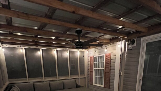 Una terraza al aire libre con banca y mesa integradas, vigas de madera y un ventilador de techo.