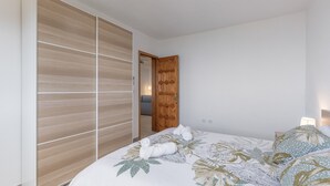 A bedroom with a bed, a wooden wardrobe, and a door leading to another room.