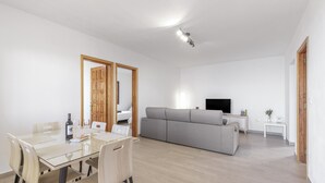 A modern living room with a glass dining table, grey sofa, and a flat-screen TV.