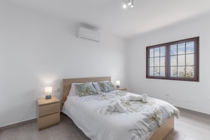 Een slaapkamer met een bed, nachtkastjes, een raam en een airconditioning.