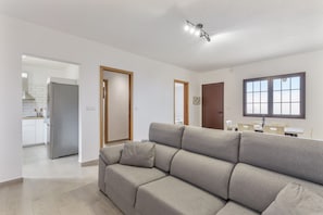 Een moderne woonkamer met een bank, een keuken op de achtergrond en een eethoek met een tafel en stoelen.