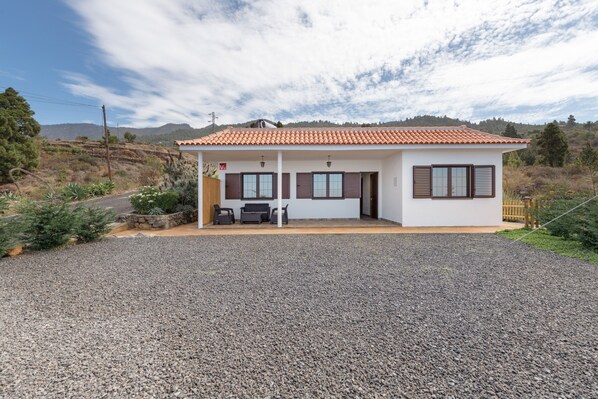 Una casa de un piso con techo de tejas, entrada de grava y un pequeño patio con mobiliario exterior.