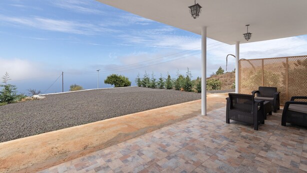 An outdoor patio with a view of the sea, a pergola, and wicker furniture.