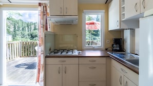 A compact kitchen with a gas stove, a coffee maker, and a view of the deck. - Mobile Home 'Le Chataignier' with Shared Pool, Private Terrace and Private Garden (Saint-Pompon)
