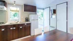 A modern kitchen with a built-in stove, sink, and refrigerator, a dining table with chairs, and a sliding glass door leading to a balcony.