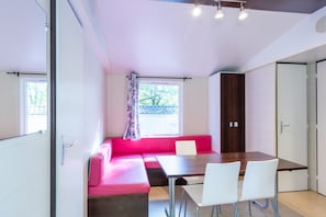 A modern room with a dining table, white chairs, a pink sofa, and a window with a view. - Mobile Home 'Le Cocon' with Shared Pool, Private Terrace and Wi-Fi (Saint-Pompon)