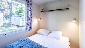 A bedroom with a bed, a window, a curtain, and a wall-mounted shelf.