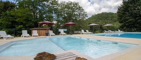 A swimming pool with lounge chairs and umbrellas, surrounded by trees.