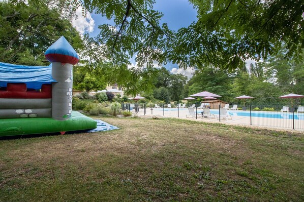 Un patio trasero con piscina, castillo inflable y sillas de descanso.