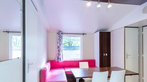 Una habitación moderna con una mesa de comedor, sillas blancas, un sofá rosa y un ventanal con vistas.