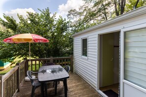 A small deck with a table and chairs, an umbrella, and a sliding glass door leading to a room. - Mobile Home 'Le Chene' with Shared Pool, Private Terrace and Private Garden (Saint-Pompon)
