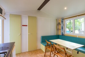 A compact kitchen with a stove, a bench, and a table. - Mobile Home 'Le Chene' with Shared Pool, Private Terrace and Private Garden (Saint-Pompon)