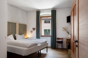 Une chambre à coucher avec un lit, une chaise, une petite table, un téléviseur et une fenêtre avec des rideaux.