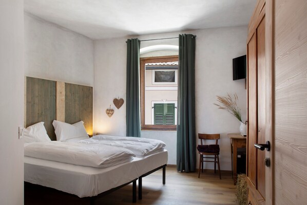 A bedroom with a bed, a chair, a small table, a TV, and a window with curtains.