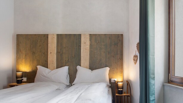 Ein Bett mit weißer Bettwäsche, einem Holz-Kopfteil, zwei Nachttischen mit Lampen und einem Fenster mit Vorhang.