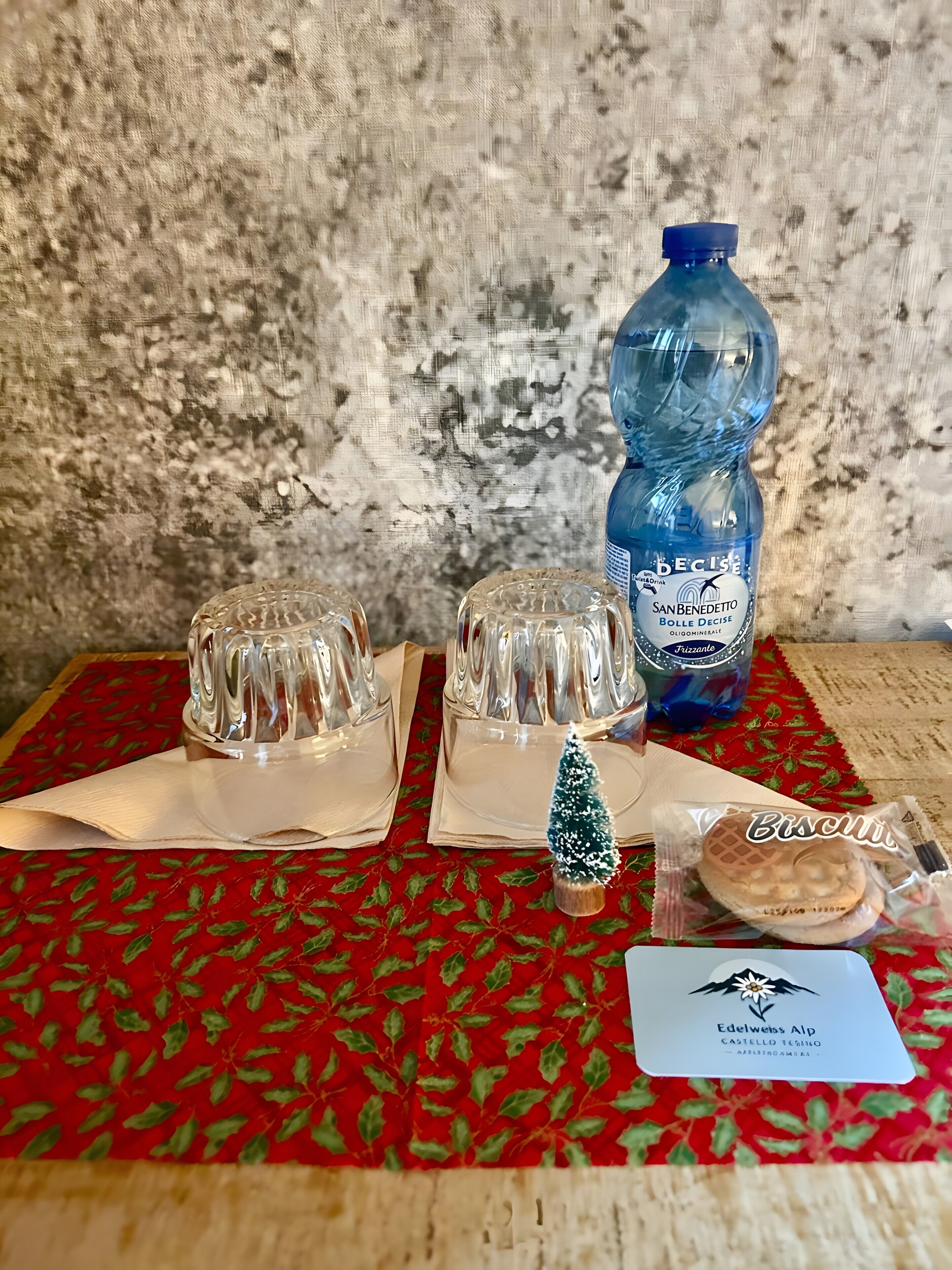 Un taulell amb sicodècs de vidre transparent, una ampolla d'aigua blava, un xicotet arbre de Nadal i un paquet de galetes.