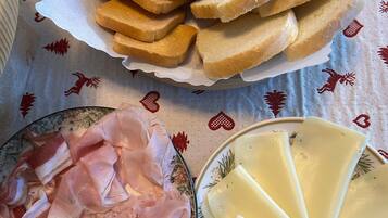 Une table avec une assiette de jambon en tranches, un bol de fromage et un panier de petits pains.
