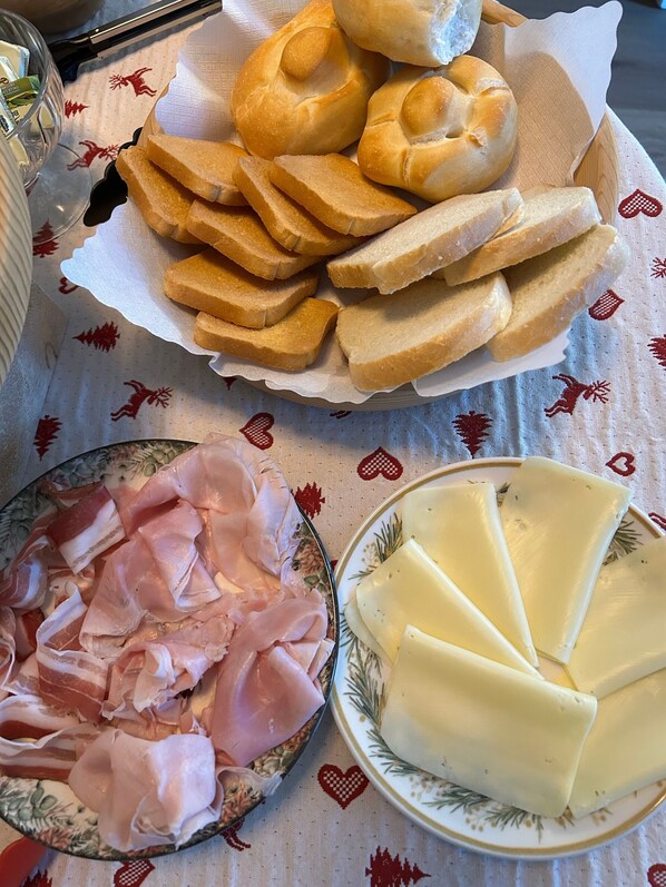 Une table avec une assiette de jambon en tranches, un bol de fromage et un panier de petits pains.