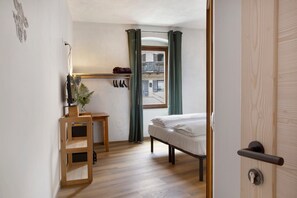A bedroom with a bed, a wooden desk, a shelf with items, a window with curtains, and a door. - Room 'Edelweiss Alp' with Mountain View and Wi-Fi (Castello Tesino)