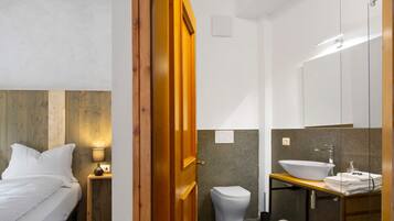 A hotel room with a bed, bedside table, lamp, wooden headboard, and a bathroom with a toilet, sink, mirror, and towel rack.