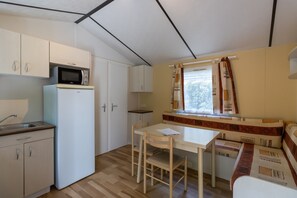 A compact kitchen with a microwave, refrigerator, and a dining area with a table and chairs. - Mobile Home 'Le Noyer' with Shared Pool, Private Terrace and Private Garden (Saint-Pompon)