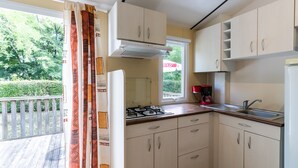 A compact kitchen with a gas stove, a sink, and light-colored cabinets. - Mobile Home 'Le Noyer' with Shared Pool, Private Terrace and Private Garden (Saint-Pompon)