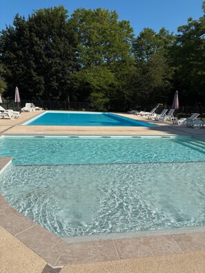 A rectangular swimming pool with clear blue water, surrounded by lounge chairs and umbrellas, set against a backdrop of trees. - Mobile Home 'Du Soleil' with Shared Pool, Private Terrace and Wi-Fi (Saint-Pompon)