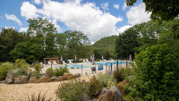 Un espace piscine agrémenté de chaises longues et de parasols, entouré de rochers et de verdure.