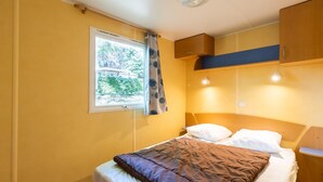 Une chambre à coucher comprenant un lit, une fenêtre avec des rideaux, une table de chevet et une armoire intégrée.