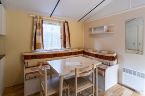 A compact kitchen with a built-in bench, a small table, and a window with curtains. - Mobile Home 'La Truffière' with Shared Pool, Private Terrace and Private Garden (Saint-Pompon)