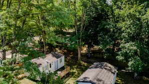 A mobile home with a fenced yard, surrounded by dense trees. - Mobile Home 'La Truffière' with Shared Pool, Private Terrace and Private Garden (Saint-Pompon)