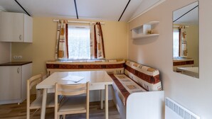 A compact room with a dining table, chairs, a bench, a window with curtains, a mirror, and a small shelf. - Mobile Home 'La Truffière' with Shared Pool, Private Terrace and Private Garden (Saint-Pompon)
