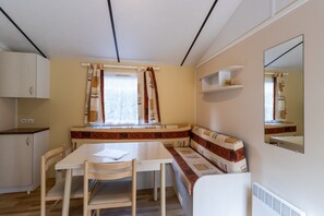 A compact room with a dining table, chairs, a bench, a window with curtains, a mirror, and a small shelf.