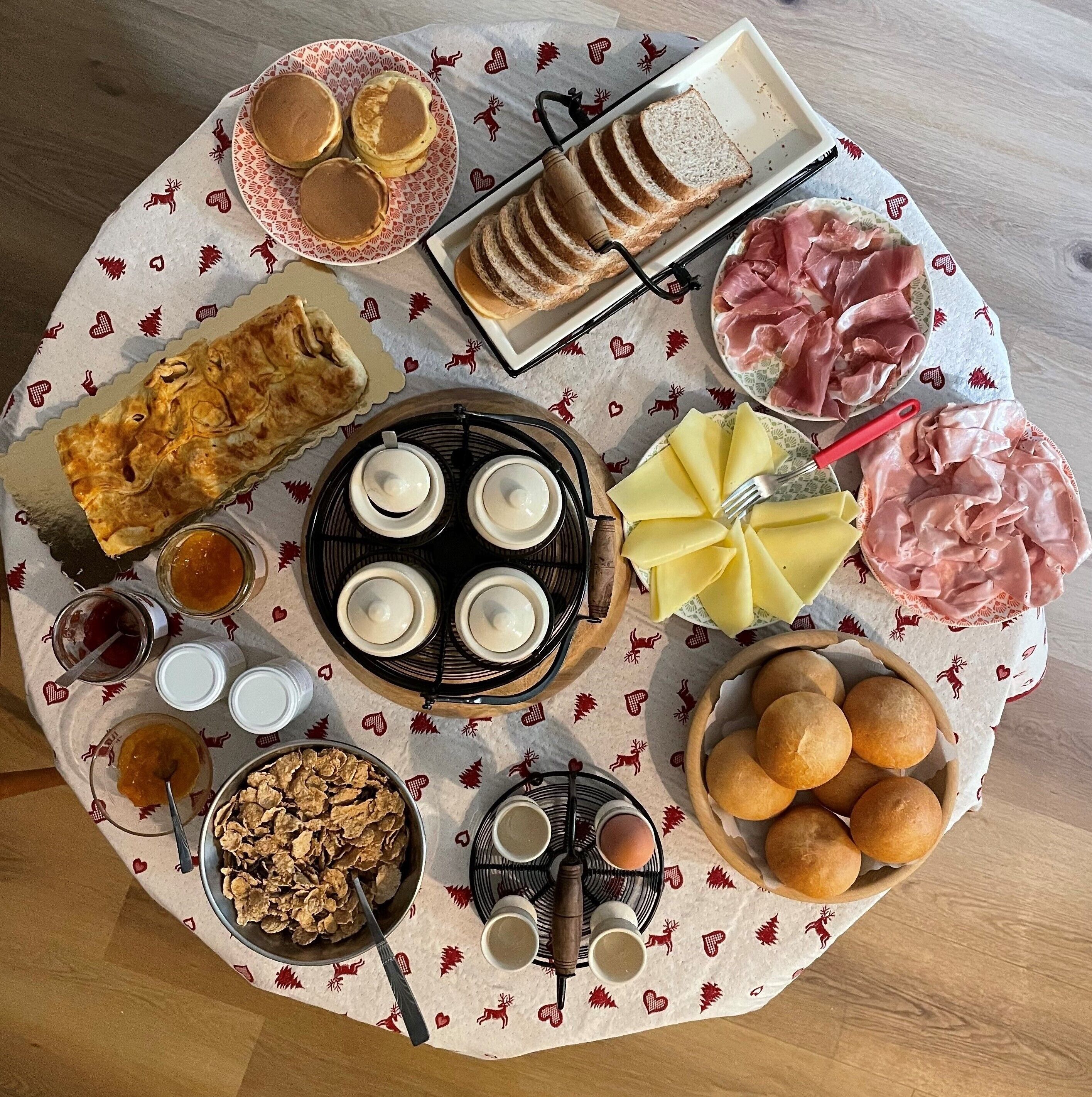 A table with various food items and utensils, including pancakes, bread, cheese, and meats.
