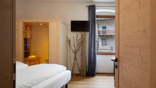 Ein Schlafzimmer mit Bett, Kleiderschrank, Fernseher und Blick auf ein Gebäude durch ein Fenster.