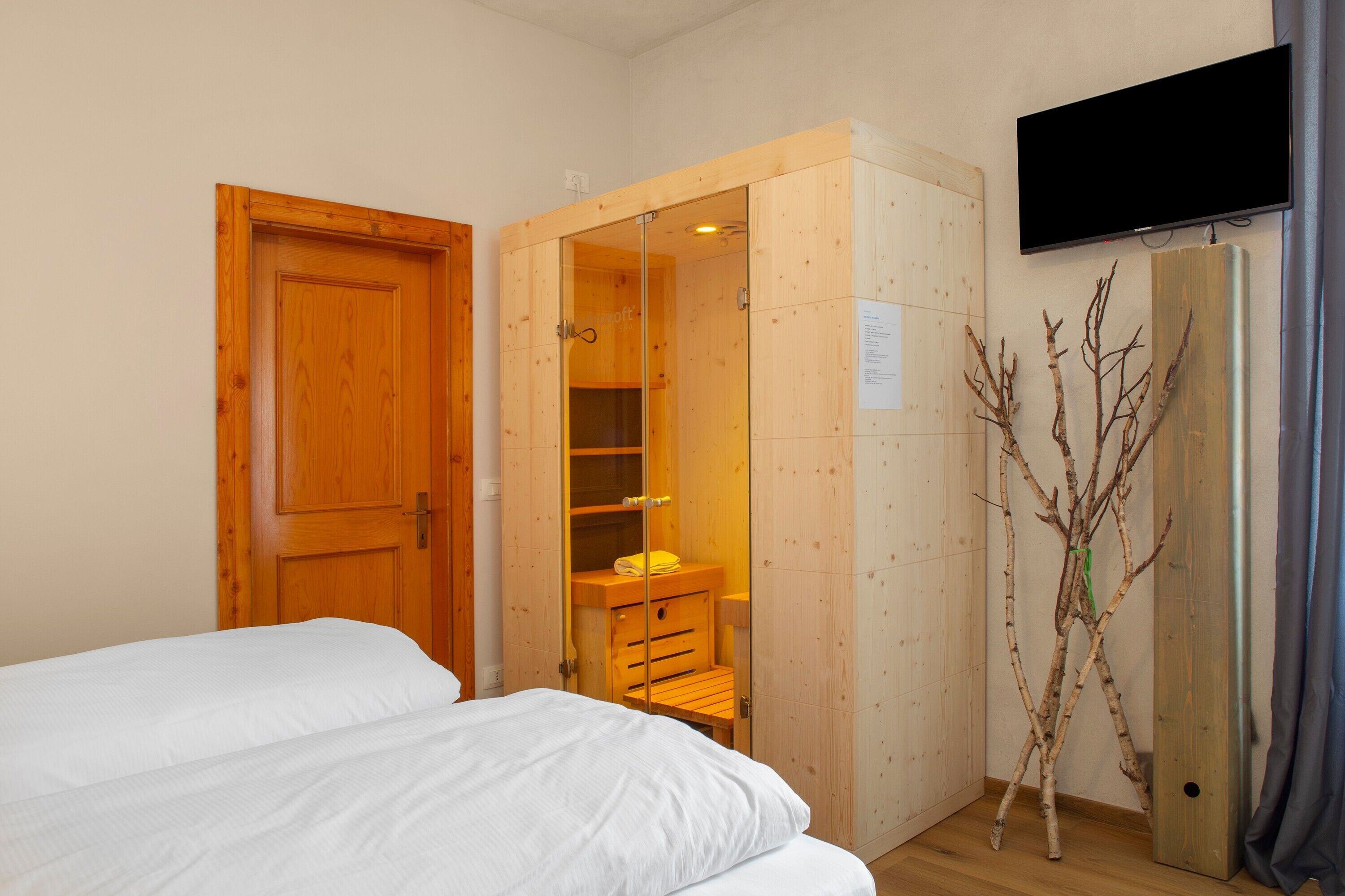 Une chambre avec une armoire en bois, un lit, un téléviseur fixé au mur et une décoration en forme de branche.