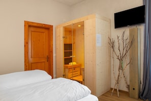A bedroom with a wooden wardrobe, a bed, a television mounted on the wall, and a branch decoration.