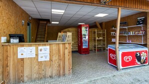 Un intérieur en bois avec un réfrigérateur Coca-Cola, un congélateur orné d’un motif en forme de cœur et une échelle menant à une porte.