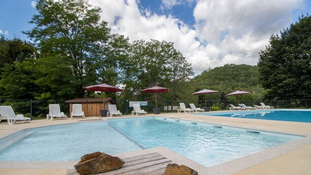 Une piscine entourée d’arbres, avec des chaises longues et des parasols.