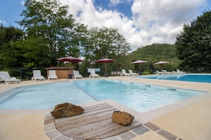A swimming pool with lounge chairs and umbrellas, surrounded by trees.