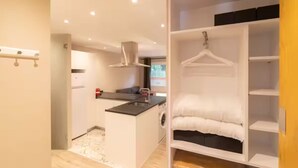 Un apartamento pequeño con kitchenette, lavadora y vestidor con estantes y espacio para colgar ropa.
