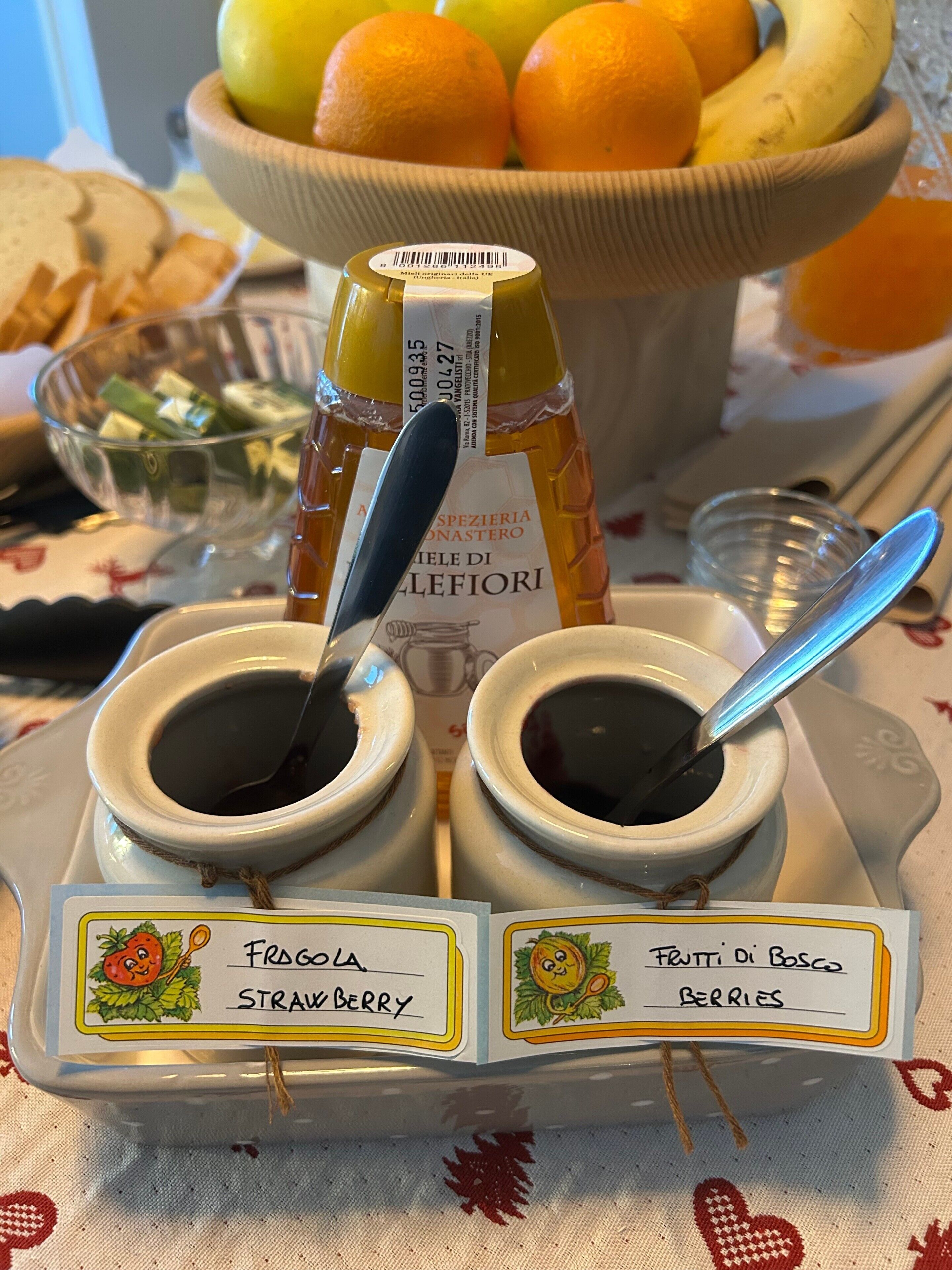 A table with two small bowls labeled 'Strawberry' and 'Berries,' a bottle of honey, and a bowl of fruit in the background.