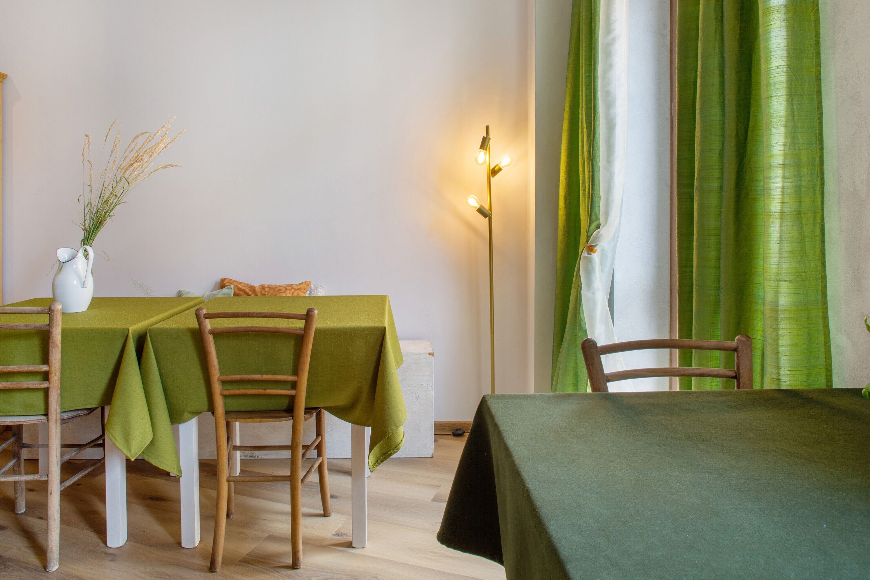 Un coin repas avec une table dressée pour quatre personnes, des chaises en bois, un vase contenant des plantes séchées et un lampadaire.