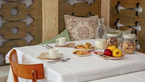 Ein Esstisch mit weißer Tischdecke, ein Holzstuhl und verschiedene Speisen, darunter ein Teller Obst, eine Karaffe und Gläser mit Granola.