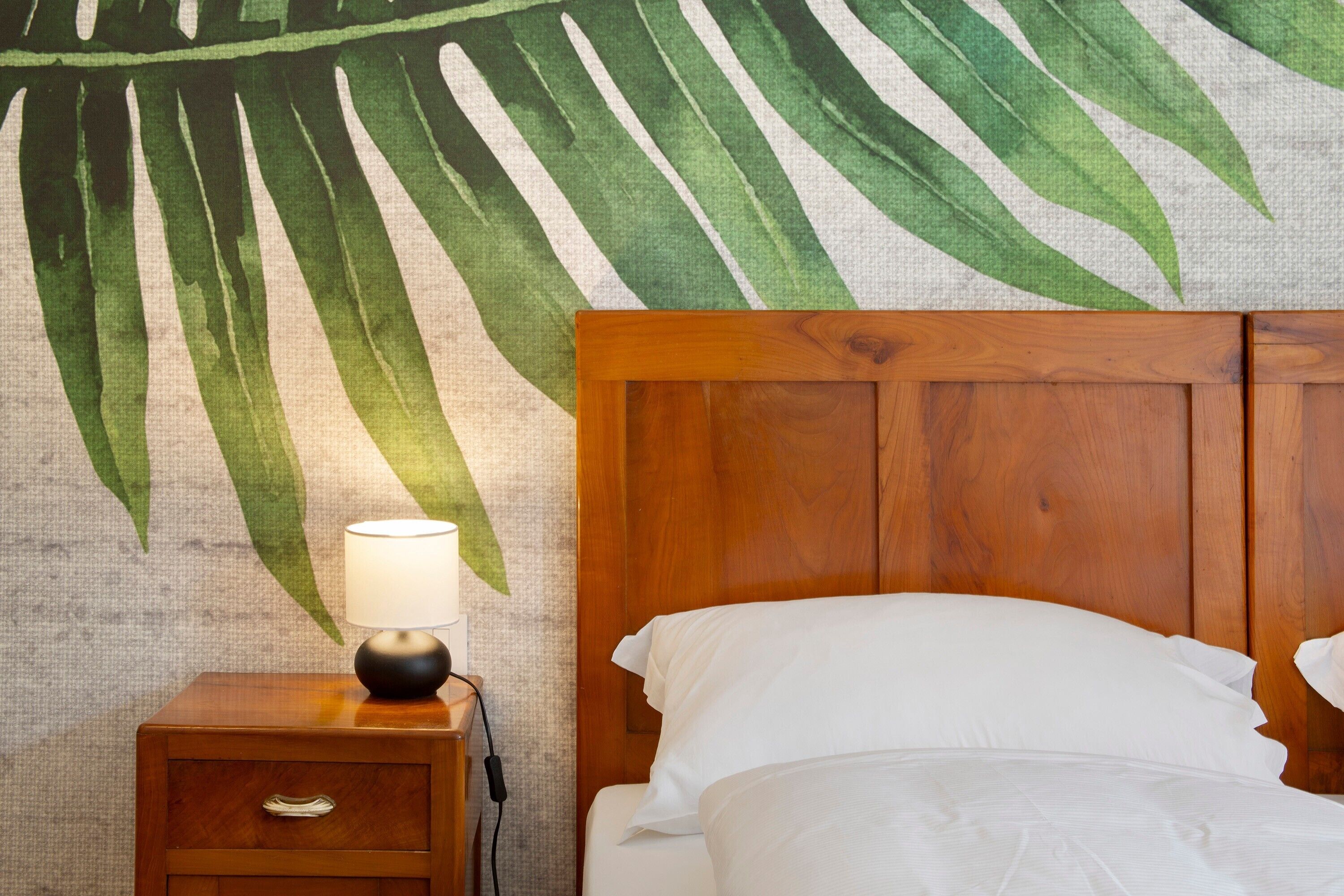 A neatly made bed with white linens, a wooden headboard, and a nightstand with a lamp.